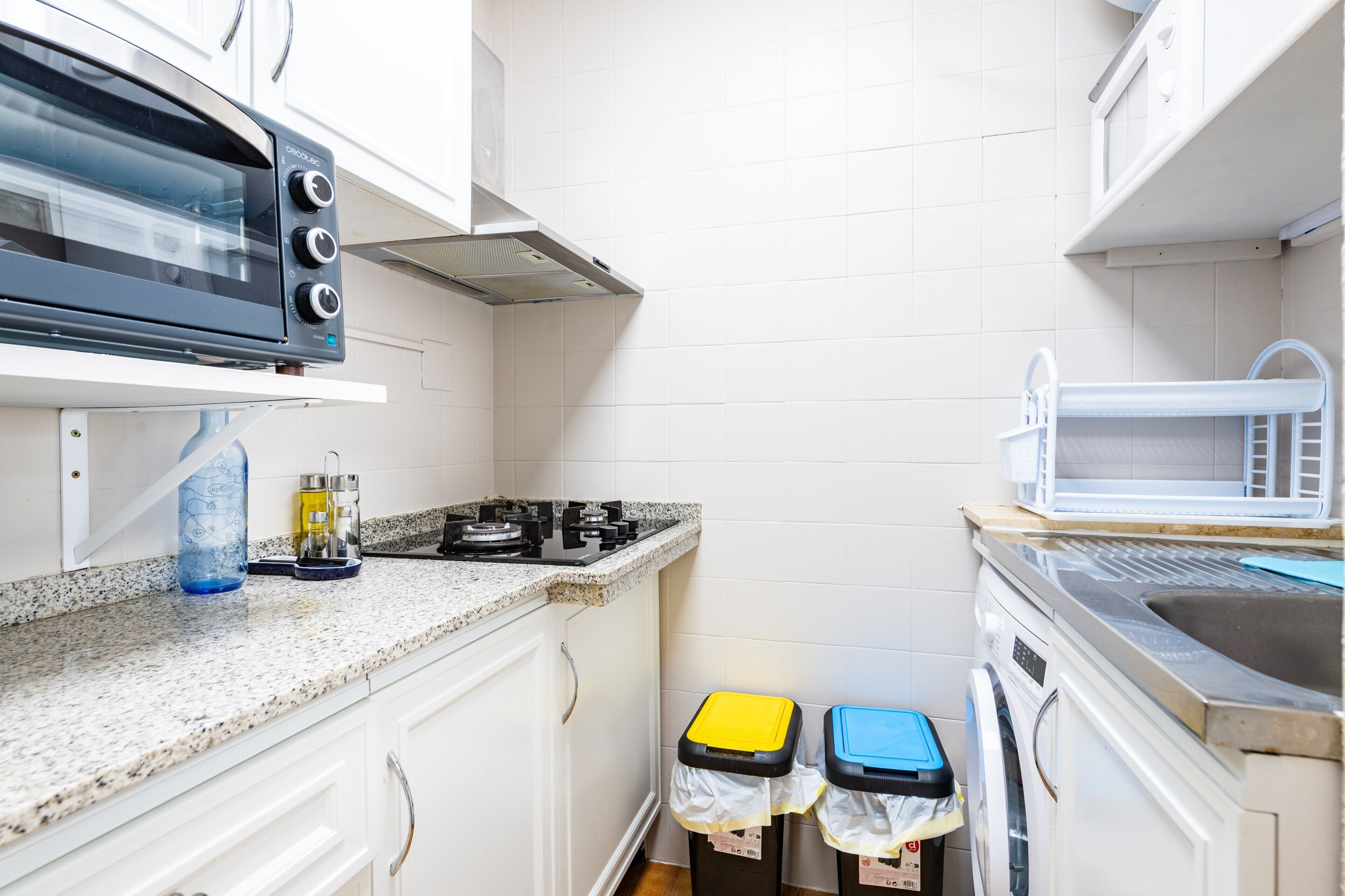 A compact kitchen with a microwave, stove, and sink. There are two trash bins and a water dispenser on the counter.