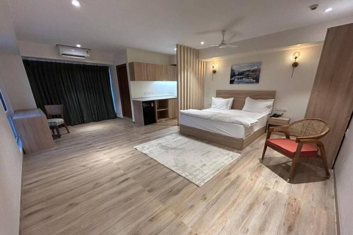 A bedroom with a bed, a desk, a chair, a TV, and a wall-mounted light.
