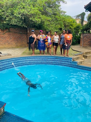A swimming pool with a tiled edge, surrounded by a brick wall and greenery.