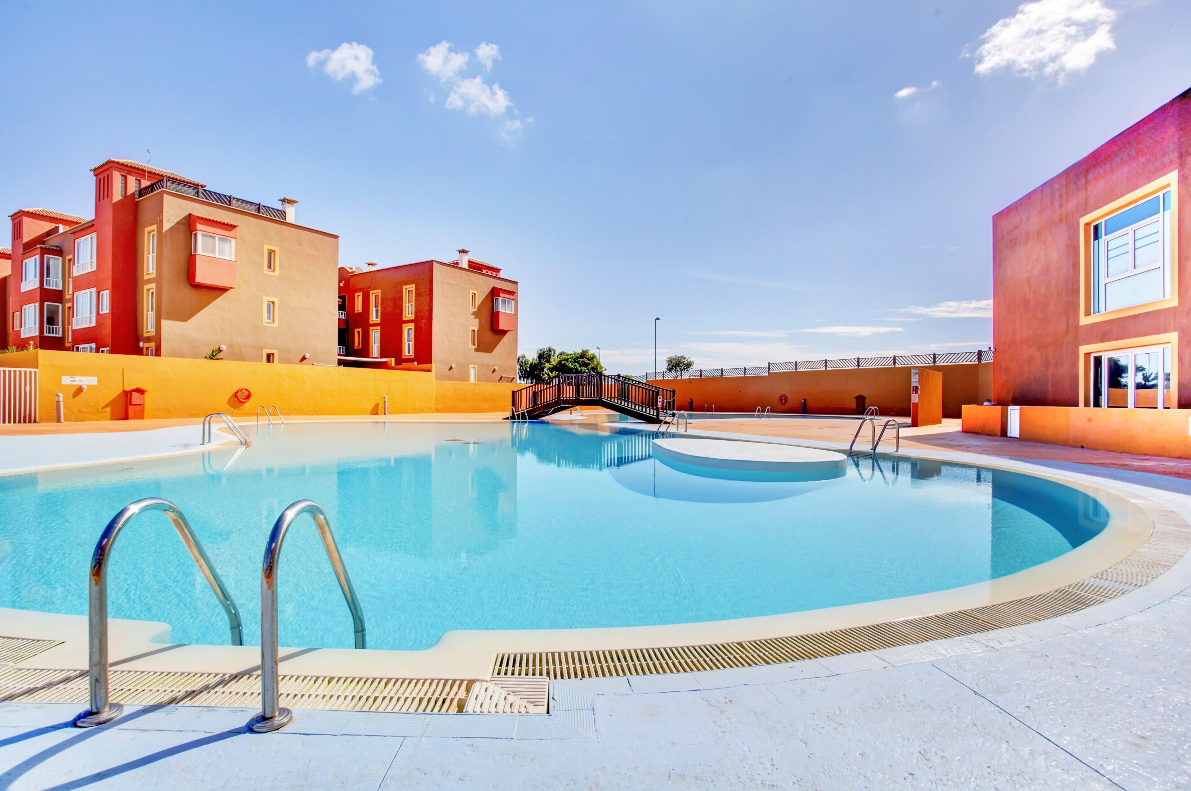A swimming pool with a metal ladder, surrounded by buildings with balconies and a clear sky.
