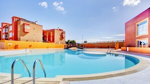 Piscina com escada de metal, rodeada por edifícios com varandas e um céu limpo.