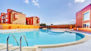 A swimming pool with a metal ladder, surrounded by buildings with balconies and a clear sky.