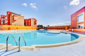 A swimming pool with a metal ladder, surrounded by buildings with balconies and a clear sky. - Holiday Home 'Salitre y Lava' with Shared Pool and Private Terrace (Corralejo)