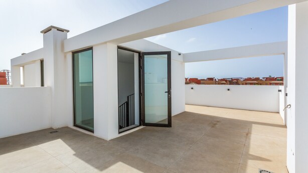 An open terrace with a glass door leading to an interior space, a tiled floor, and a clear sky in the background. - Holiday Home 'Salitre y Lava' with Shared Pool and Private Terrace (Corralejo)