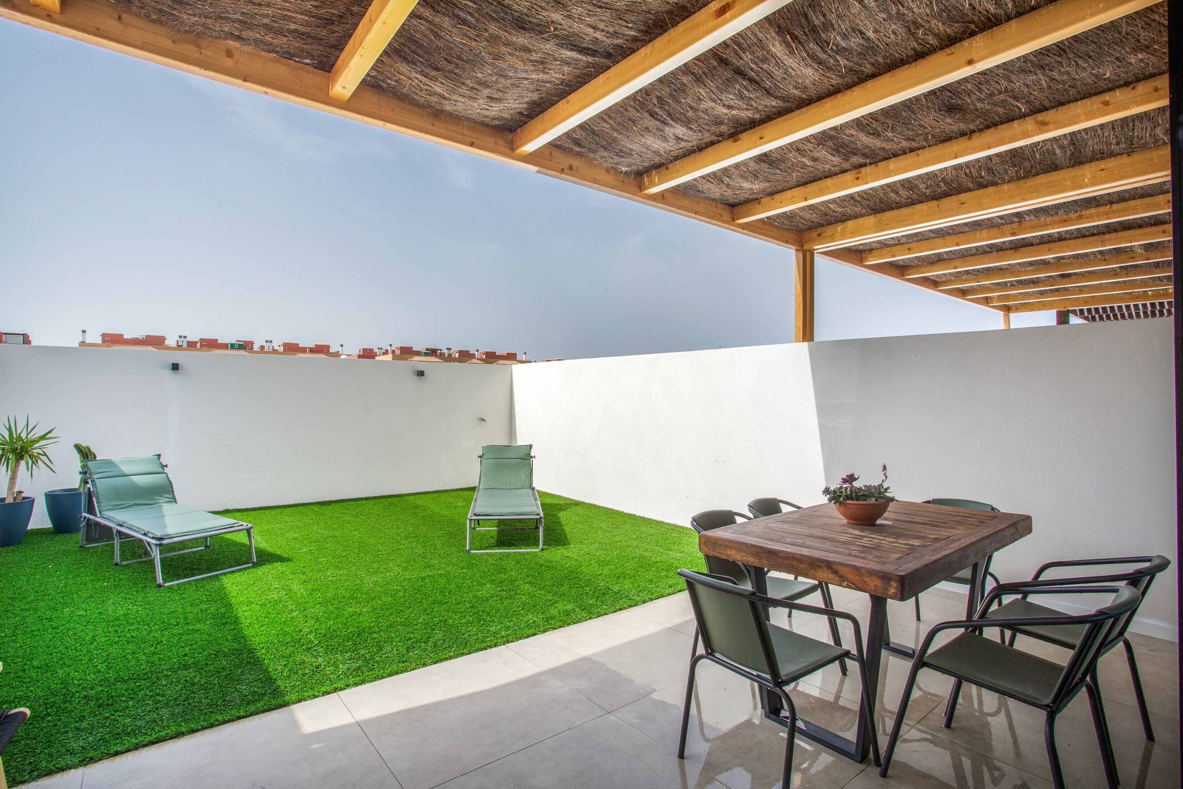 A rooftop patio with artificial grass, a table with chairs, and a pergola structure.