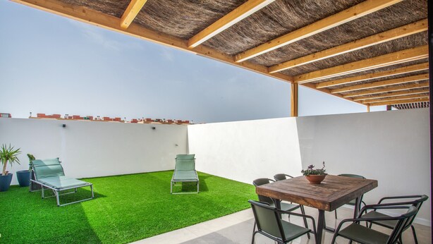 Um terraço no telhado com grama sintética, uma mesa com cadeiras e uma estrutura de pérgula.
