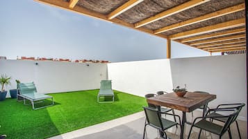 A rooftop patio with artificial grass, a table with chairs, and a pergola structure.