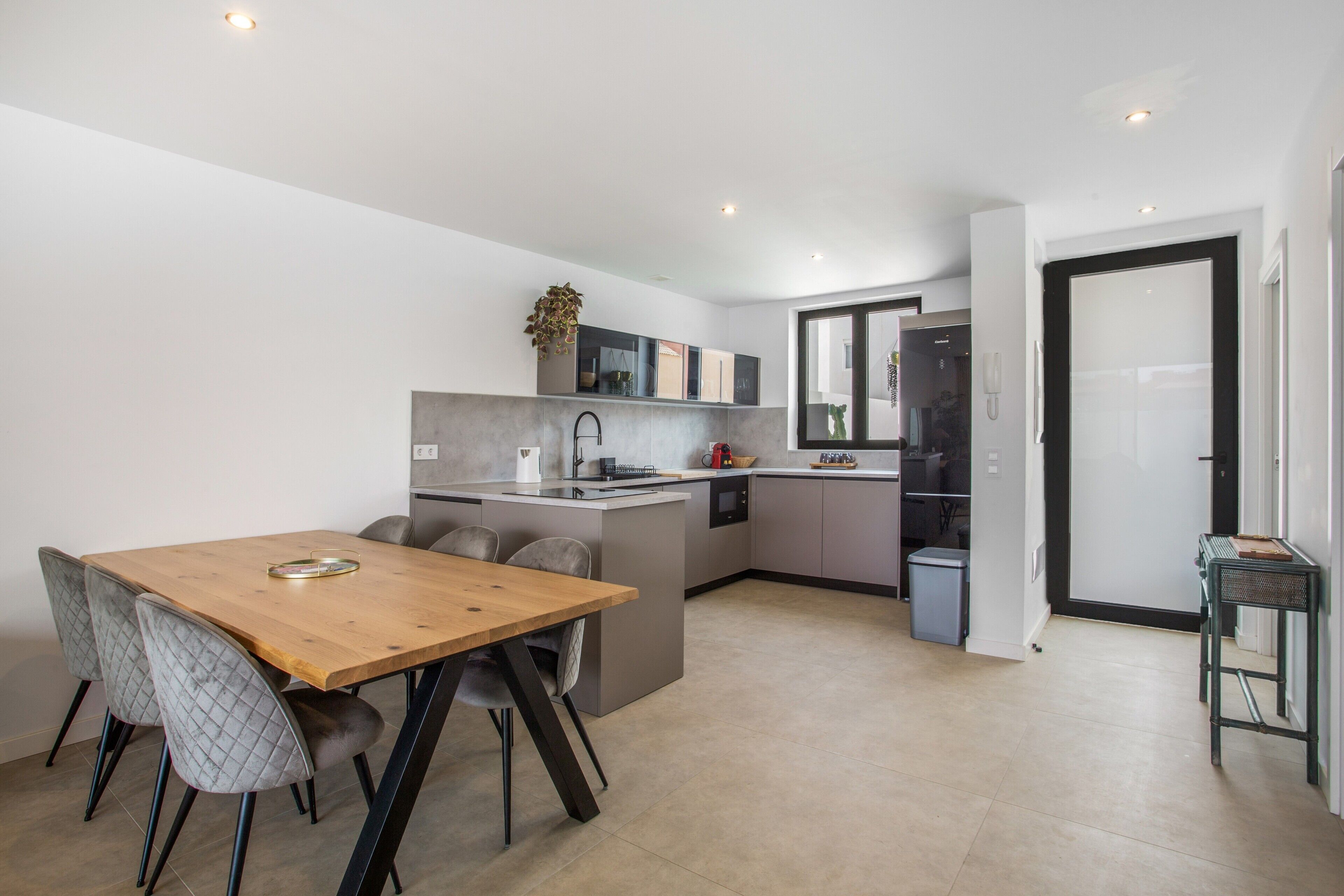 A modern kitchen with a dining area, featuring a wooden table and chairs, a built-in oven, and a small island with a sink.