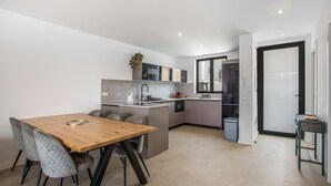 Cozinha moderna com área de jantar, apresentando uma mesa e cadeiras de madeira, forno embutido e uma pequena ilha com pia.