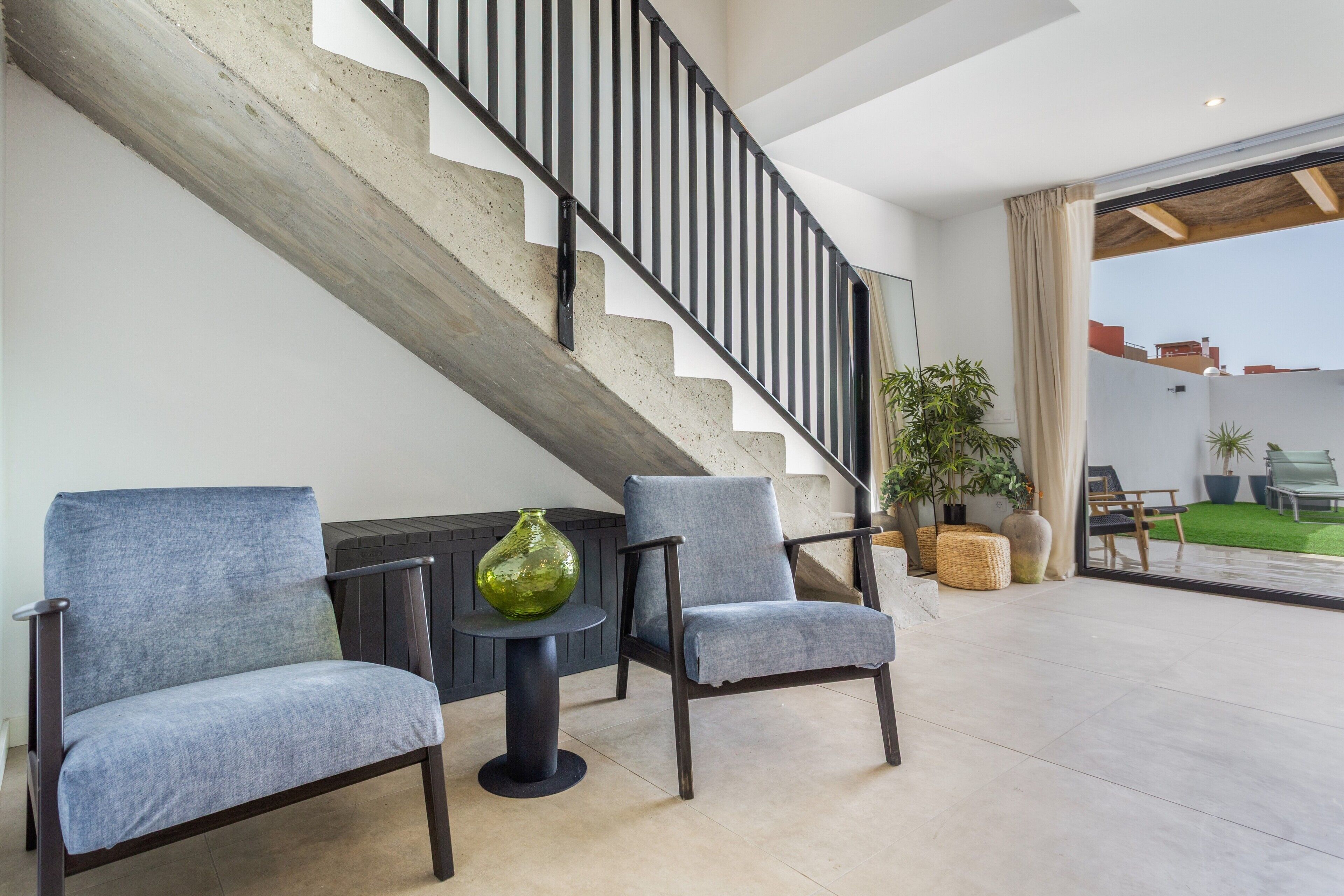 A modern interior with a staircase, two armchairs, a small table, and a green vase.