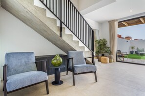 Een modern interieur met een trap, twee fauteuils, een klein tafeltje en een groene vaas.