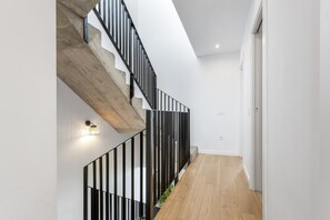 A modern staircase with black railings, a wooden floor, and a wall-mounted light fixture.