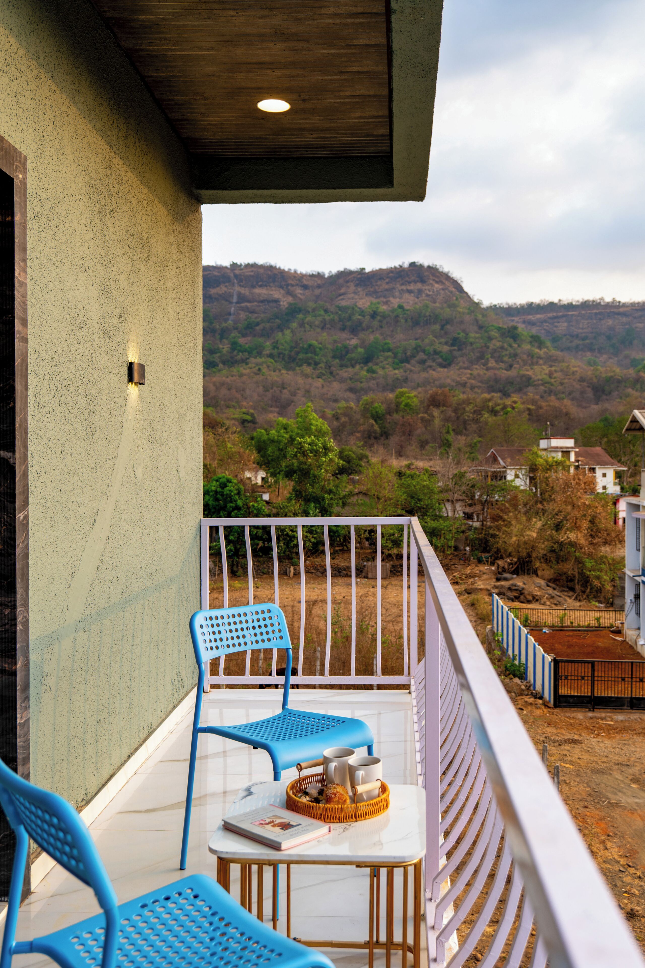 Ein Balkon mit blauen Stühlen, einem kleinen Tisch und Blick auf eine hügelige Landschaft.