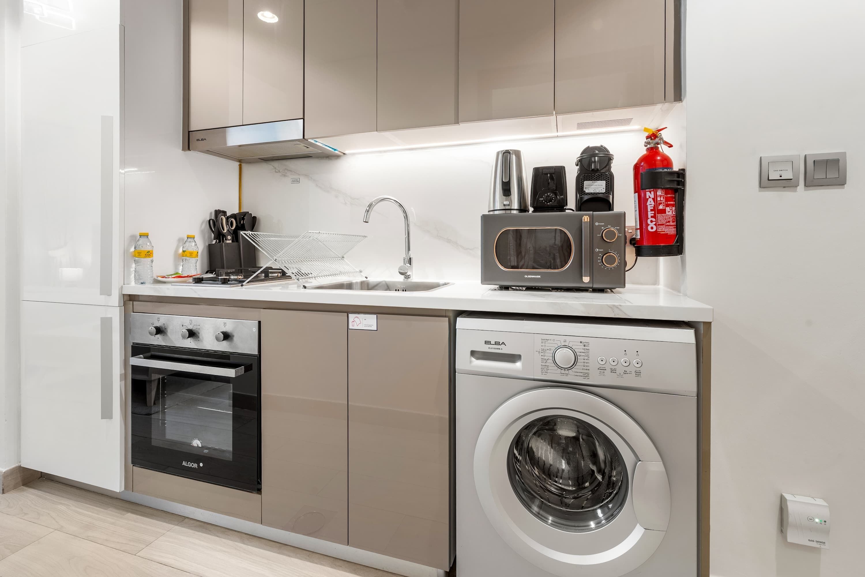 A compact kitchen with a built-in oven, microwave, and washing machine, a sink, and a fire extinguisher.