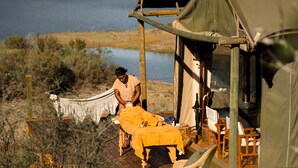 A tent with a table and chairs outside, a hammock, and a person sitting on the ground.