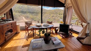 A cozy interior with a wooden table, chairs, a bookshelf, and a view of a mountainous landscape.