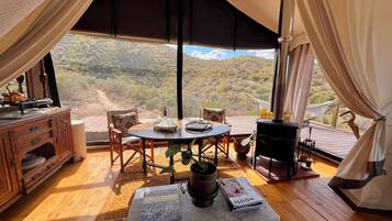 Um interior acolhedor com uma mesa de madeira, cadeiras, uma estante e vista para uma paisagem montanhosa.