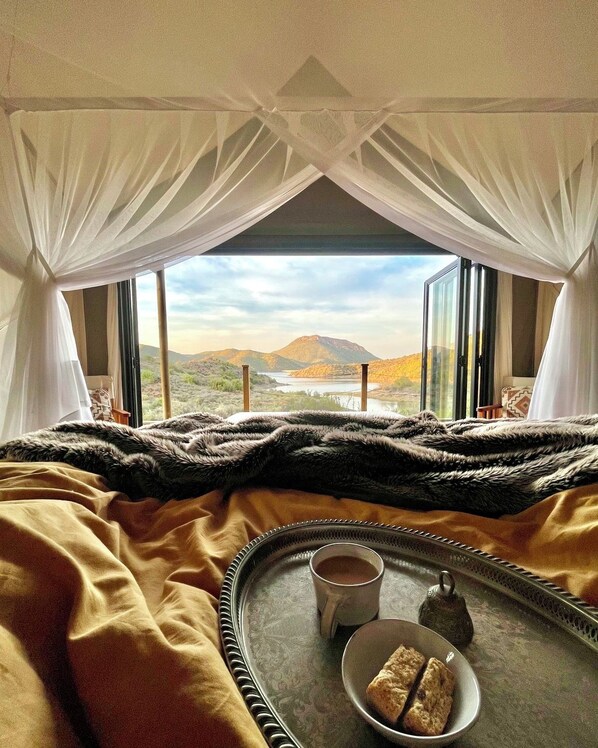 A bed with a view of a mountainous landscape through large windows.