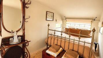 Quarto com cama de madeira, um espelho grande, uma mesinha com bandeja e um tapete estampado.