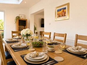 A dining table set for six with plates, glasses, and a centerpiece of white flowers. - Spacious Corby House  Sleeps 8  Patio & BBQ (Corby)
