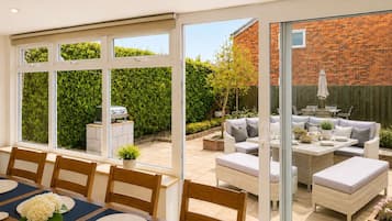 Un comedor con mesa dispuesta para cuatro, una parrilla afuera y un patio con mobiliario de exterior.