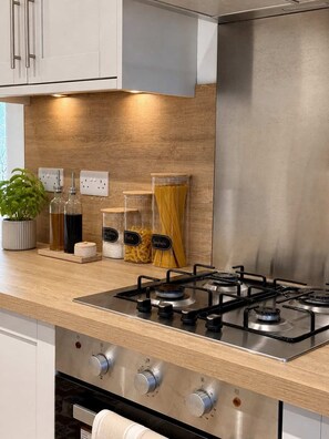 A modern kitchen with a stainless steel stove, wooden countertop, and jars labeled with pasta types. - Spacious Corby House | Sleeps 8 | Patio & BBQ (Corby)