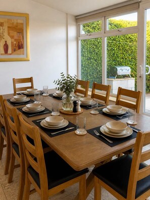 A dining area with a large table set for six, surrounded by wooden chairs with black cushions. - Spacious Corby House | Sleeps 8 | Patio & BBQ (Corby)