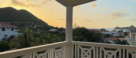 A covered balcony with a view of a mountainous landscape and buildings in the distance.