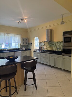 Una cocina moderna con una isla central, taburetes de bar, horno empotrado y ventana con cortinas.