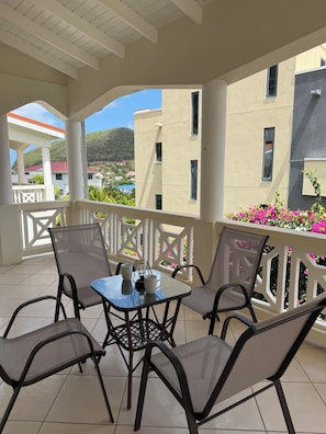 A covered outdoor seating area with a table and chairs, a view of buildings and greenery, and a white railing. - 5BR Rodney Bay Villa. Walk to Beach, Dining & Nightlife. Sleeps 10 (Gros Islet)
