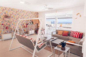 A modern living room with a swing chair, a sofa with colorful cushions, a bookshelf, and a view of the sea. - Villa Macatia - 200m from the beach (Saint-Paul)