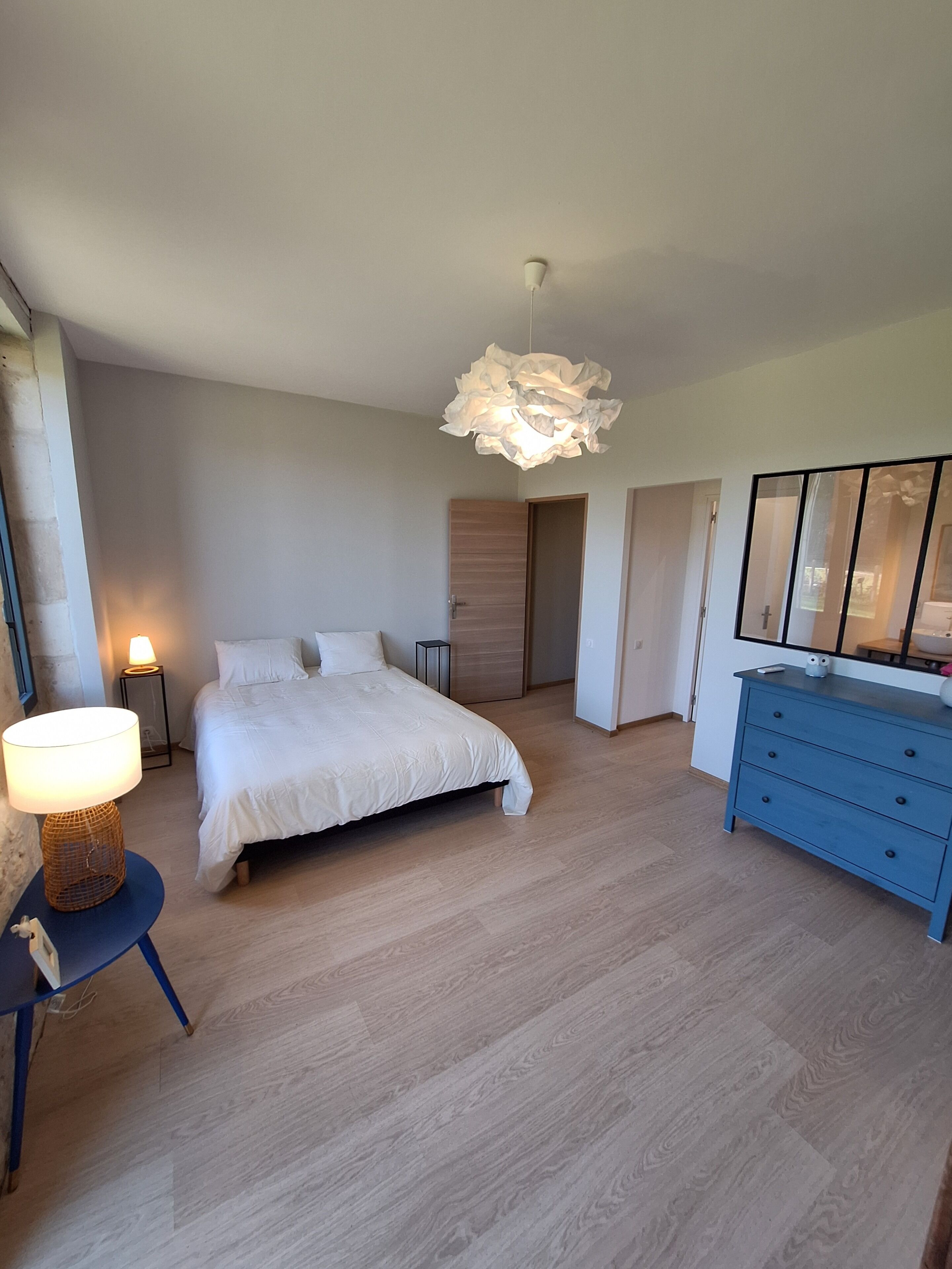 A bedroom with a bed, bedside table, lamp, dresser, and a hanging light fixture.
