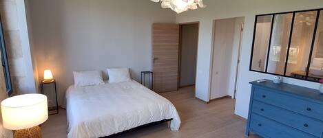 A bedroom with a bed, bedside table, lamp, dresser, and a hanging light fixture.