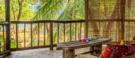 A wooden deck with a bench and cushions, overlooking a tropical landscape with palm trees.