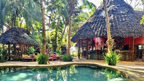 Un área de piscina con estructuras de techo de paja, rodeada de palmeras y follaje.