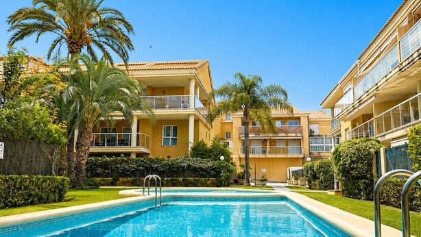 Una piscina circondata da un edificio con balconi, palme e cielo sereno.