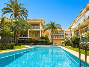 Une piscine entourée d’un bâtiment doté de balcons, de palmiers et surplombant un ciel dégagé.