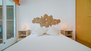 Una camera da letto con un letto grande, due comodini con lampade, un elemento decorativo sopra il letto e una porta scorrevole in vetro a sinistra.