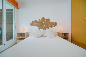 Ein Schlafzimmer mit einem großen Bett, zwei Nachttischen mit Lampen, einem Wandbild über dem Bett und einer Schiebetür aus Glas links.