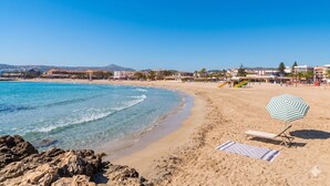 Una spiaggia con acque cristalline blu, una riva sabbiosa, un ombrellone e una sedia a sdraio.