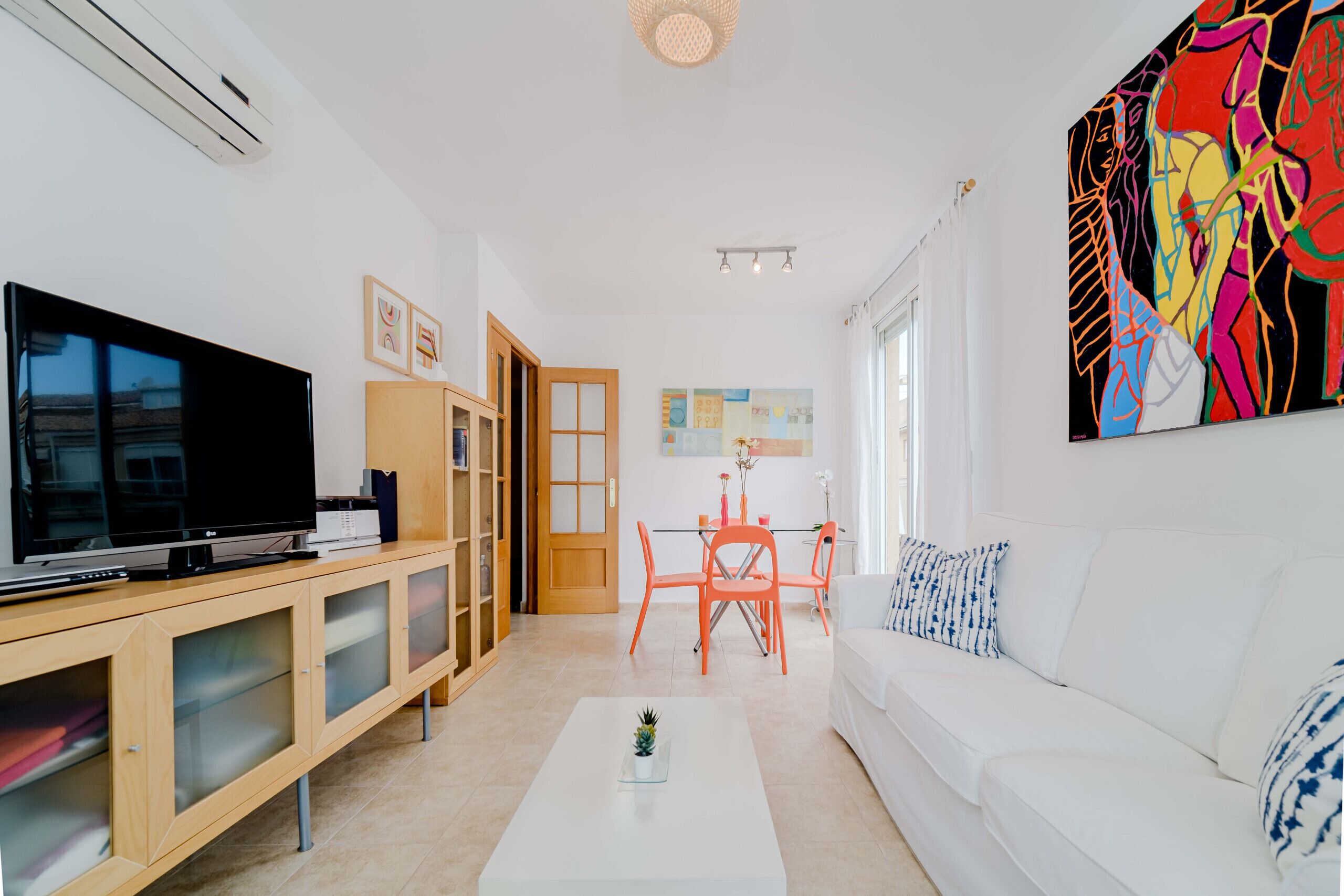 Una sala de estar moderna con un televisor de pantalla plana, mueble de madera para entretenimiento, sofá blanco y un cuadro abstracto y colorido.