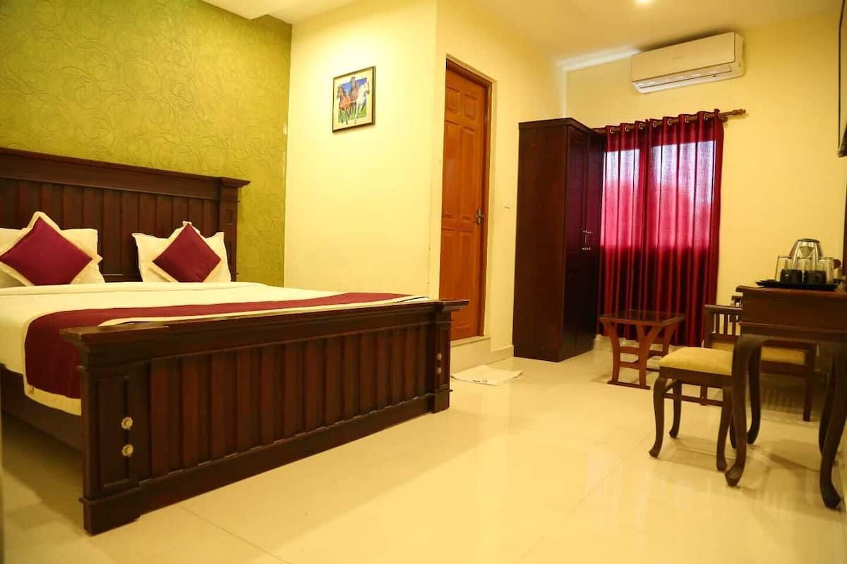 A hotel room with a bed, a desk, a chair, an air conditioning unit, and a door.