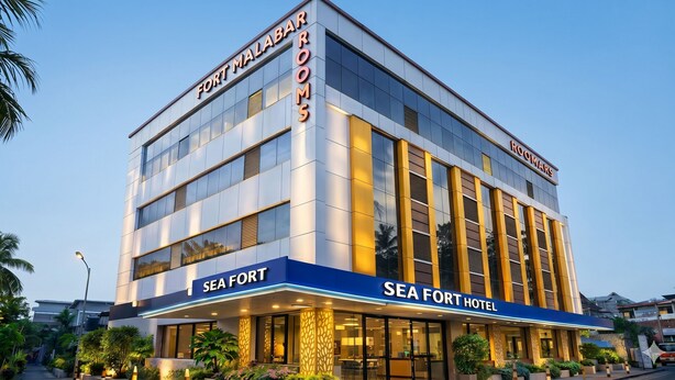 Ein mehrstöckiges Hotel mit den Schildern 'FORT MALABAR ROOMS' und 'SEA FORT HOTEL', großen Fenstern und einem gut beleuchteten Eingang.