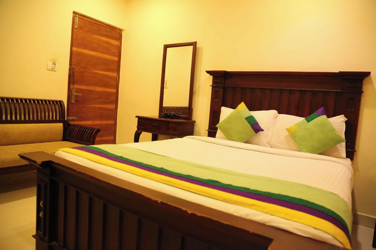 A bed with a striped blanket, a wooden headboard, a bedside table with a mirror, and a wooden bench.