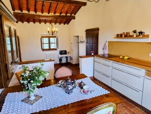 A kitchen with wooden beams, white cabinets, a dining table with a placemat, and a small table with a microwave. - Charming Apartment in the Tuscan Countryside surrounded by olive groves (CASTIGLION FIORENTINO)