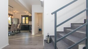 A modern interior with a staircase, a dining area with chairs, and a kitchen visible through an open doorway. - Villa Dani by Villas Guide (Gostinjac)
