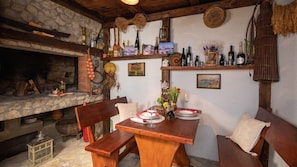 A rustic dining area with a stone fireplace, wooden benches, and a variety of bottles on shelves. - Rural house Janjic by Villas Guide (Plina Jezero)