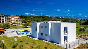 Un edificio moderno con zona de piscina, rodeado de vegetación y montañas al fondo.