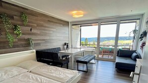 A modern bedroom with a bed, a desk, and a balcony with a view.