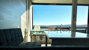 A modern room with a view of a body of water, a pool, and a wooden deck.
